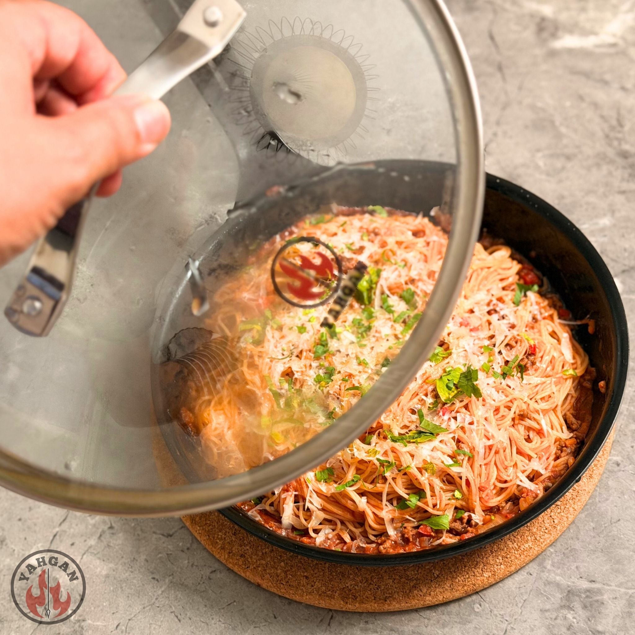 Yahgan glass lid being lifted from carbon steel pan revealing golden finished dish — oven-to-table cooking