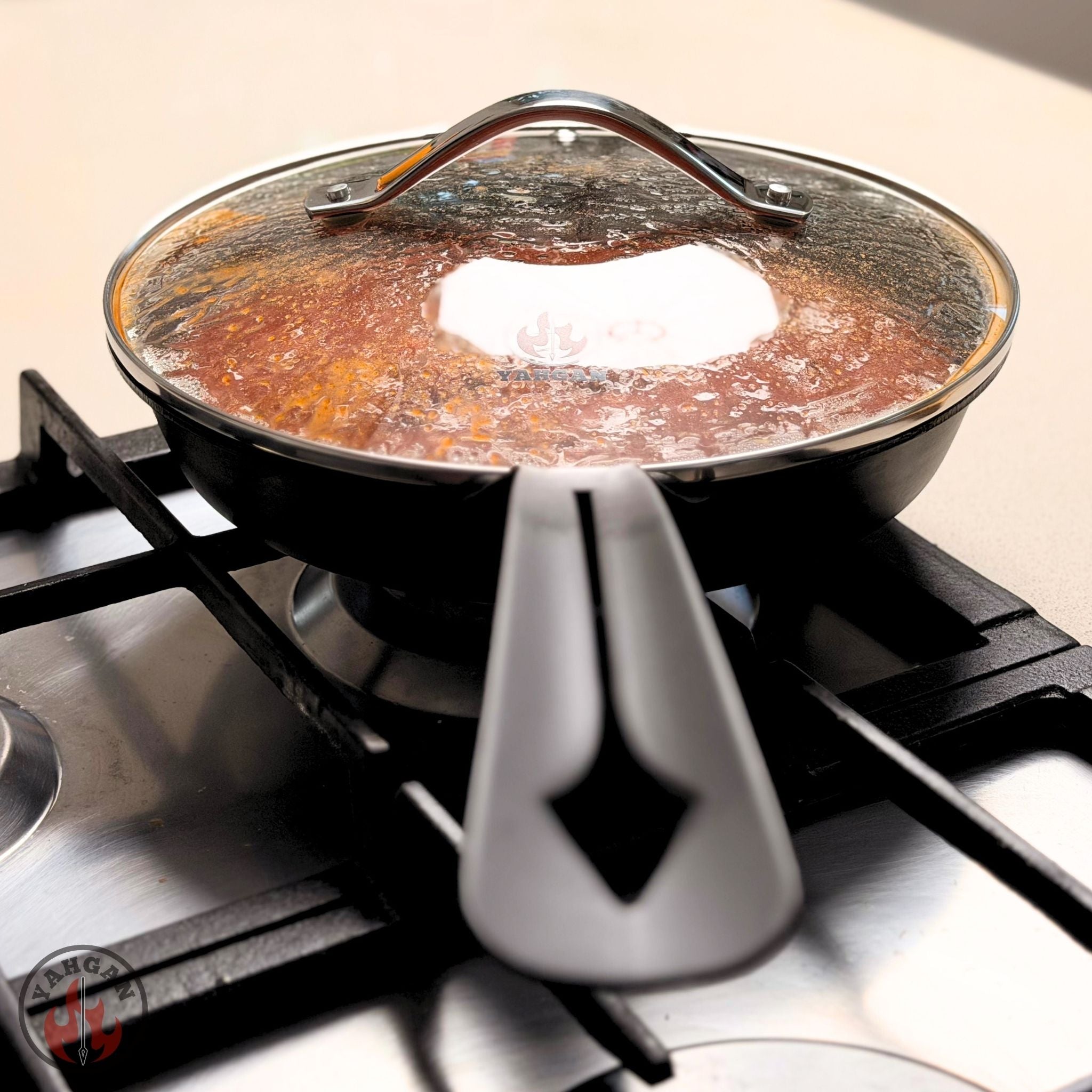 Yahgan tempered glass lid on 26cm carbon steel pan on gas stovetop — braising and steam retention in use
